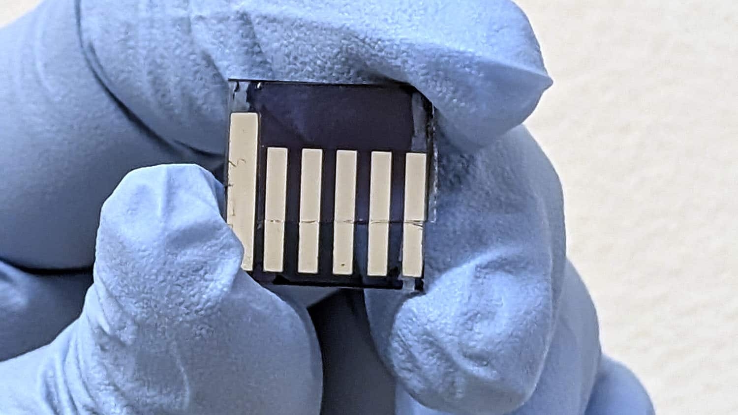 a hand wearing a latex glove holds six tiny metal strips, each only millimeters wide and no longer than a thumbnail.