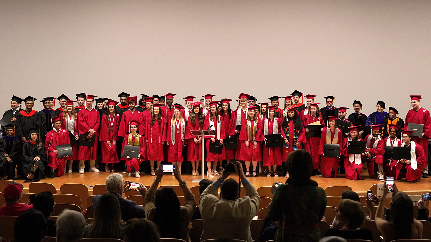 undergraduate college students onstage wearing red caps and gowns