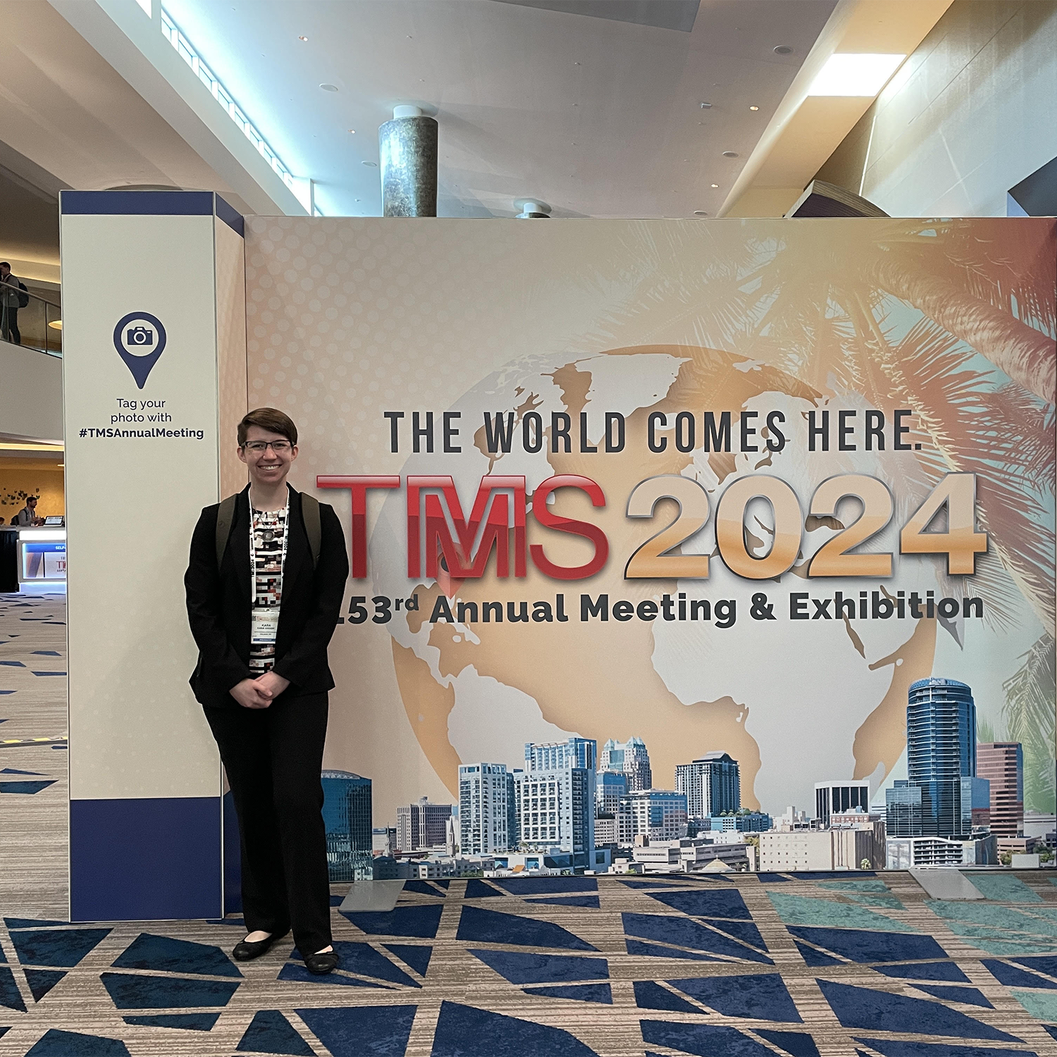 short haired brunette college woman in front of a conference waysign
