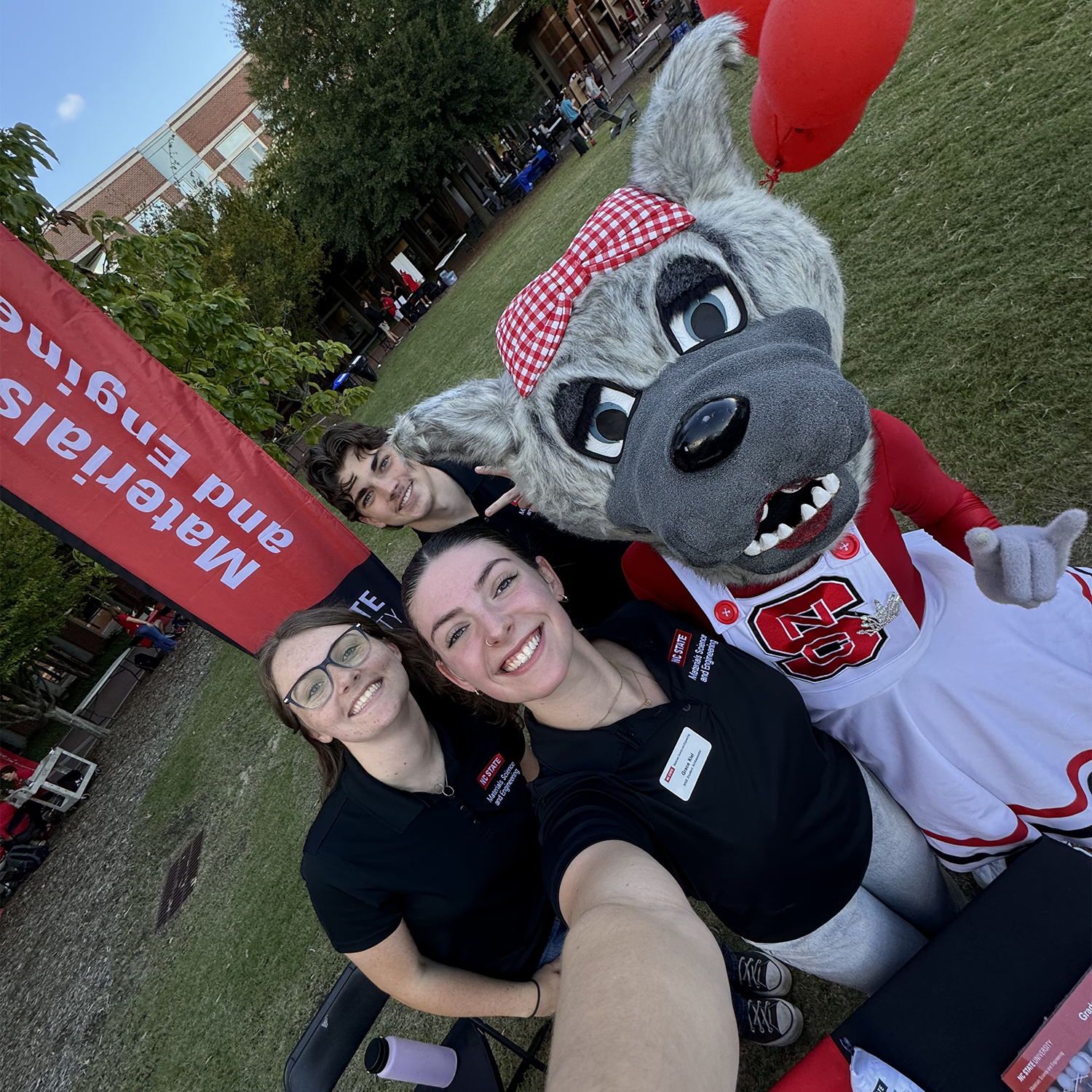 three college students pose with a wolf college mascot smiling
